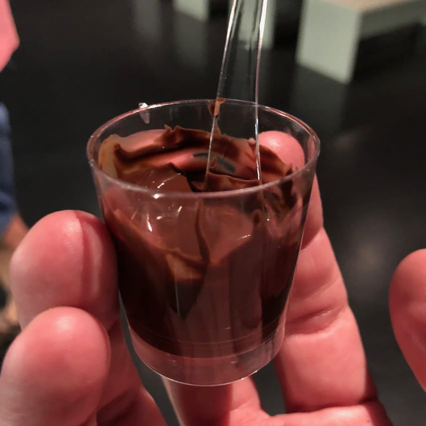 A glass with fresh, melted chocolate is held in the hand by a guest