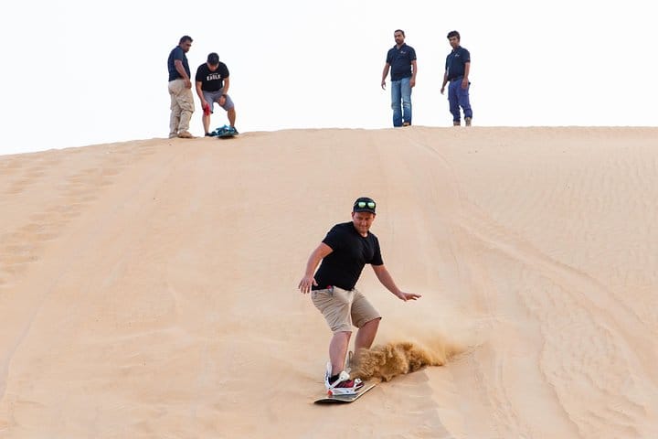 Travelers ride sand boards on the dunes near Dubai.