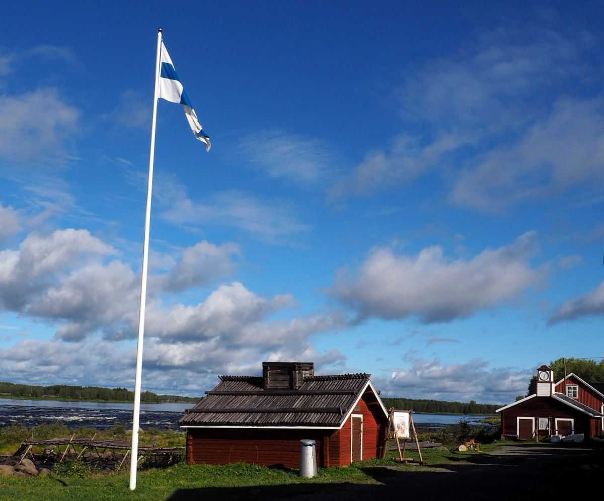 A couple of traditional red houses by the river and a Finnish flag