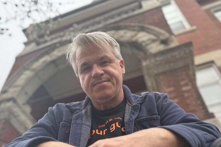 Smiling tour guide standing in front of an arched stone doorway in St. Louis Central West End