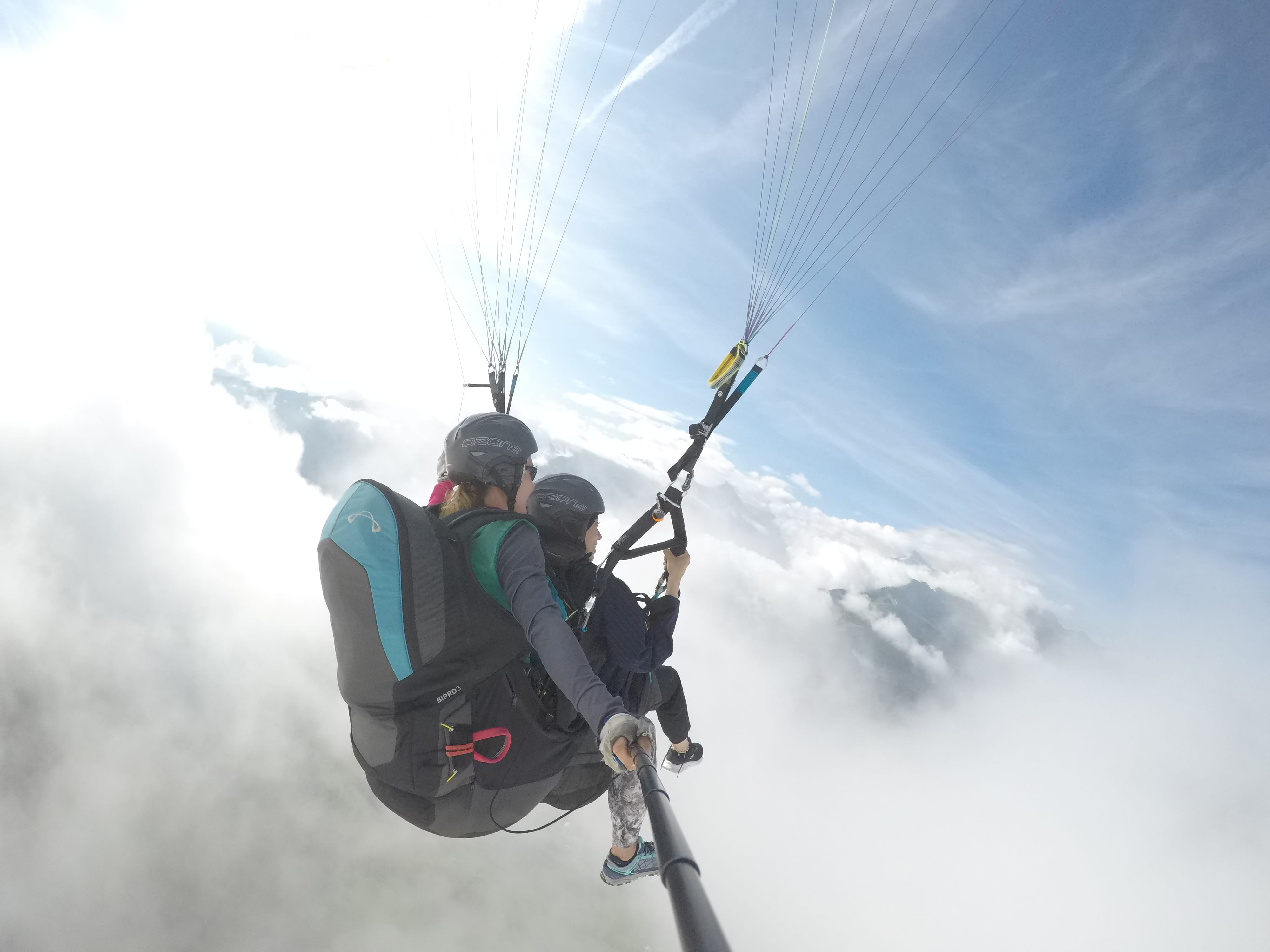 A female tandem pilot and her passenger emerging from a cloud, revealing a mountain view
