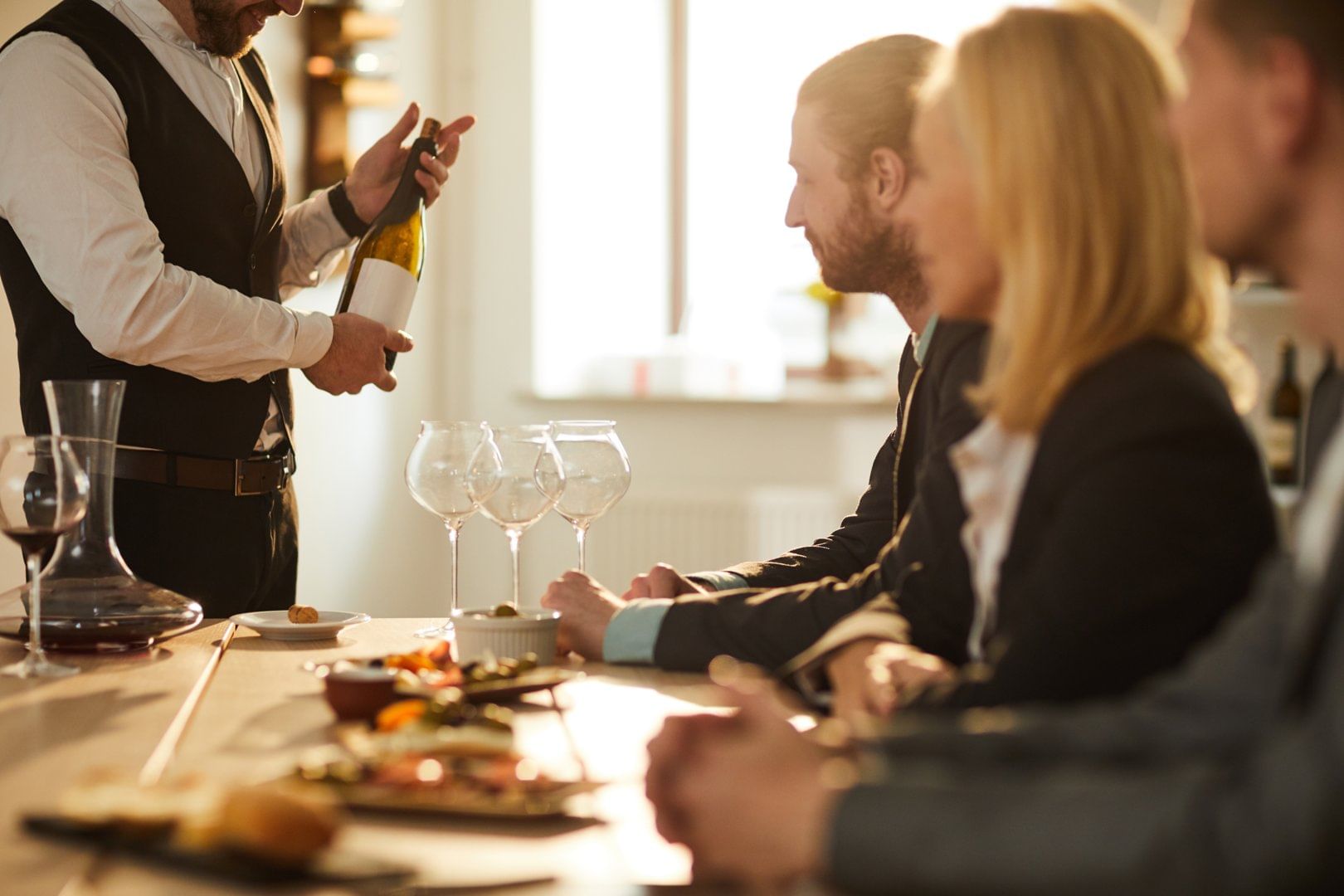 A group of people seated at a table enjoying a wine tasting session, as a sommelier pours wine and explains the selection in a cozy atmosphe