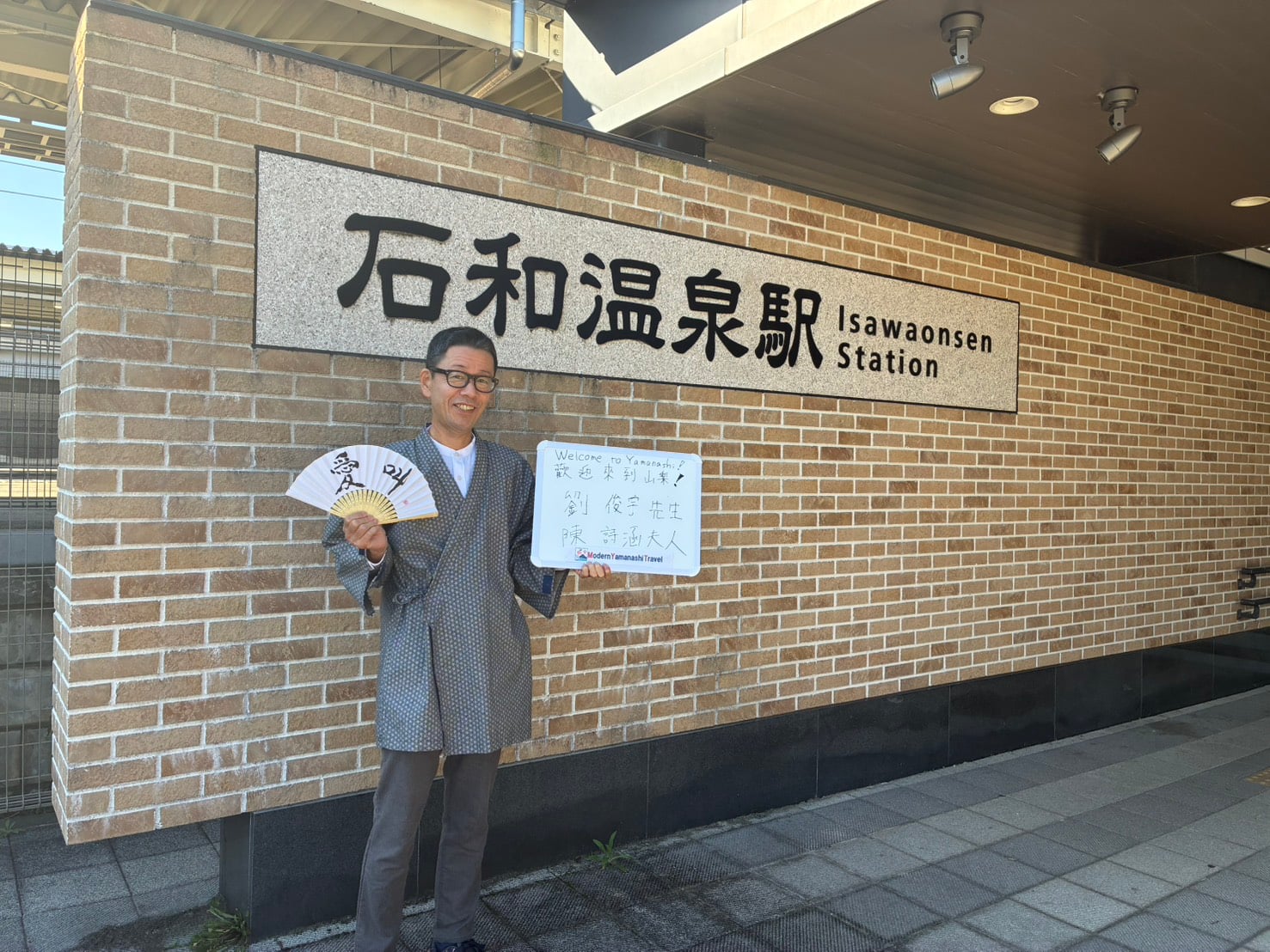 Tour guide holding a welcome sign in front of the elevator at Isawa-Onsen Station North Exit.