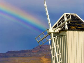 A rainbow and mountain scenery behind a wooden historic windmill