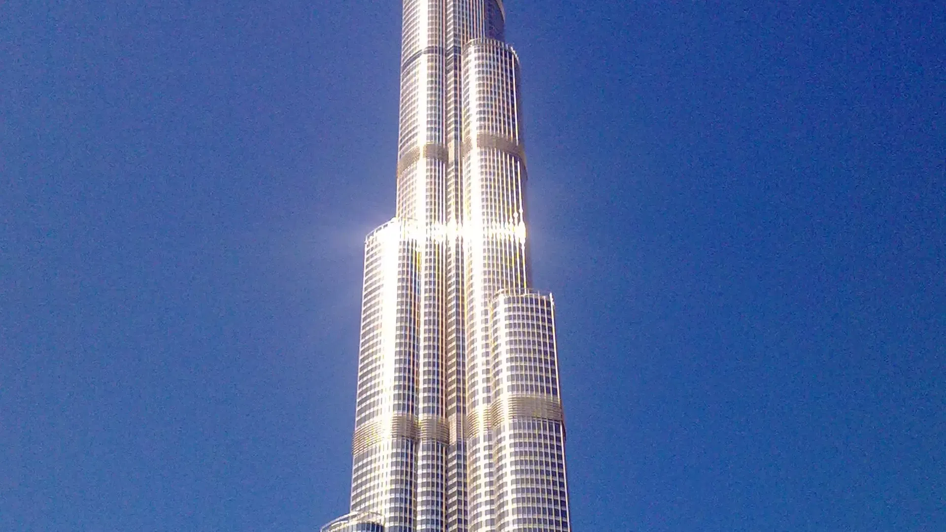The setback tiers of the tower's midsection blazing with reflected sunlight against a deep blue sky at Burj Khalifa