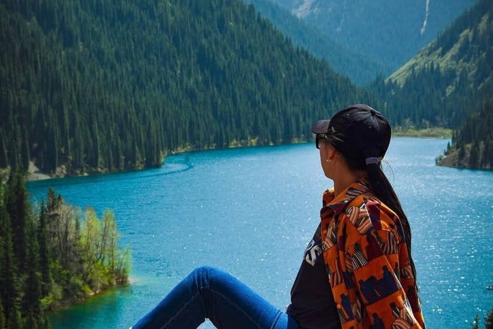 Kolsai Lake surrounded by tall pine trees and rocky mountain ridges.