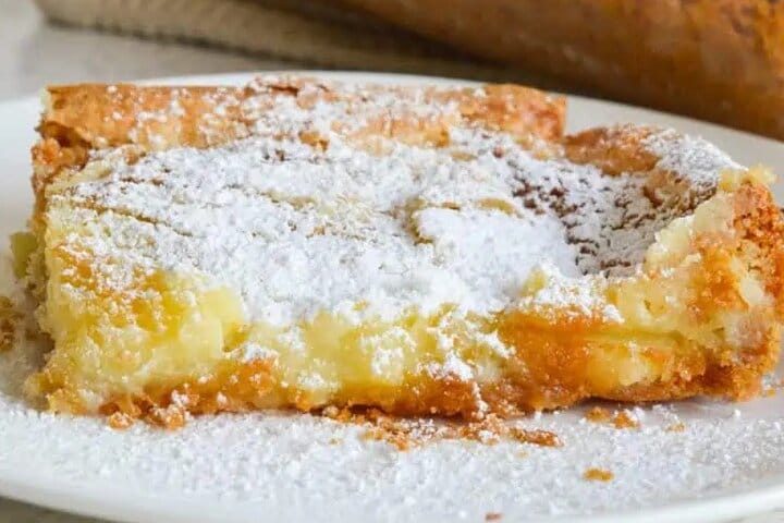 A slice of gooey butter cake dusted with powdered sugar, showing the classic dense yellow custard layer