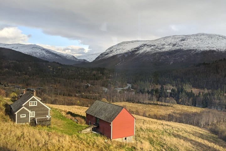 Red barn and wooden cabin beneath snow-dusted Norwegian mountains