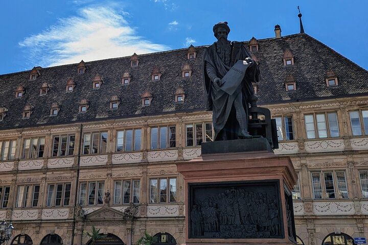 Statue de Johannes Gutenberg sur la Place Gutenberg, avec la Chambre de Commerce (Neue Bau) en arrière-plan.
