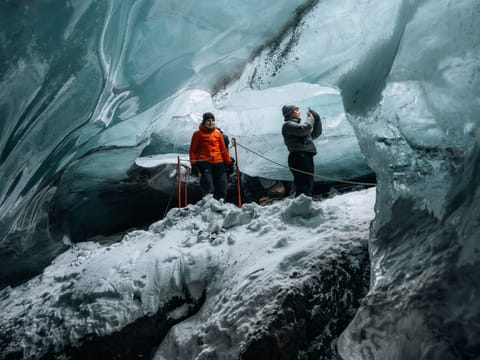 two people standing in a natural ice cave with its blue colour and shades