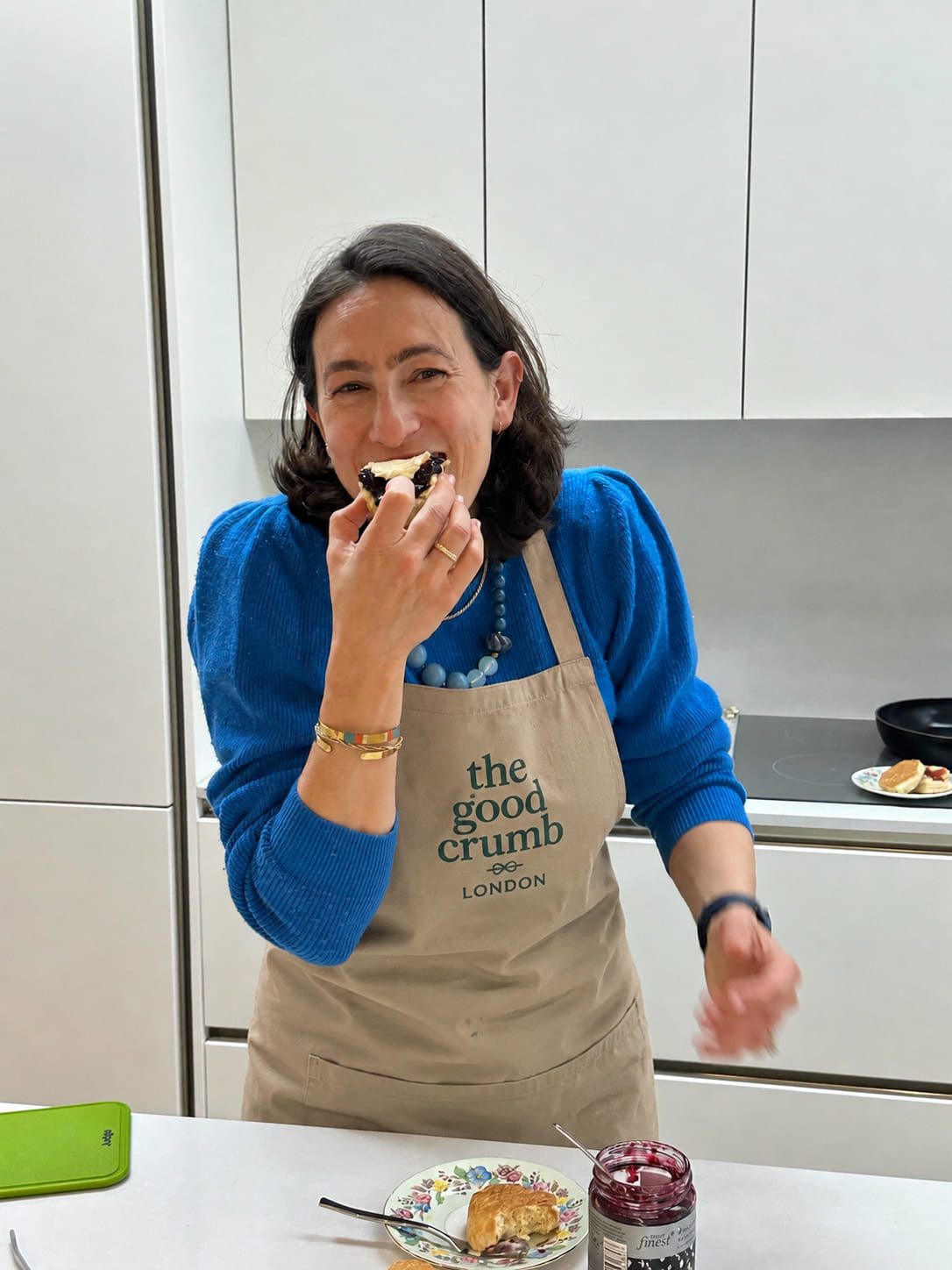A lady grinning while eating a scone laden with jam and cream