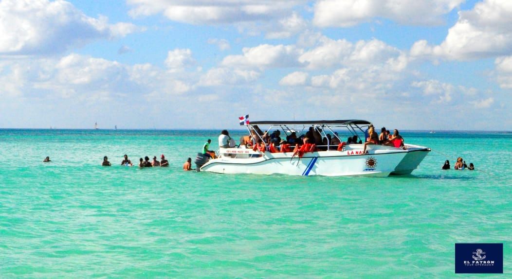 Lancha rápida repleta de visitantes flotando en las aguas turquesas de la Piscina Natural de Isla Saona, con varias personas nadando alreded