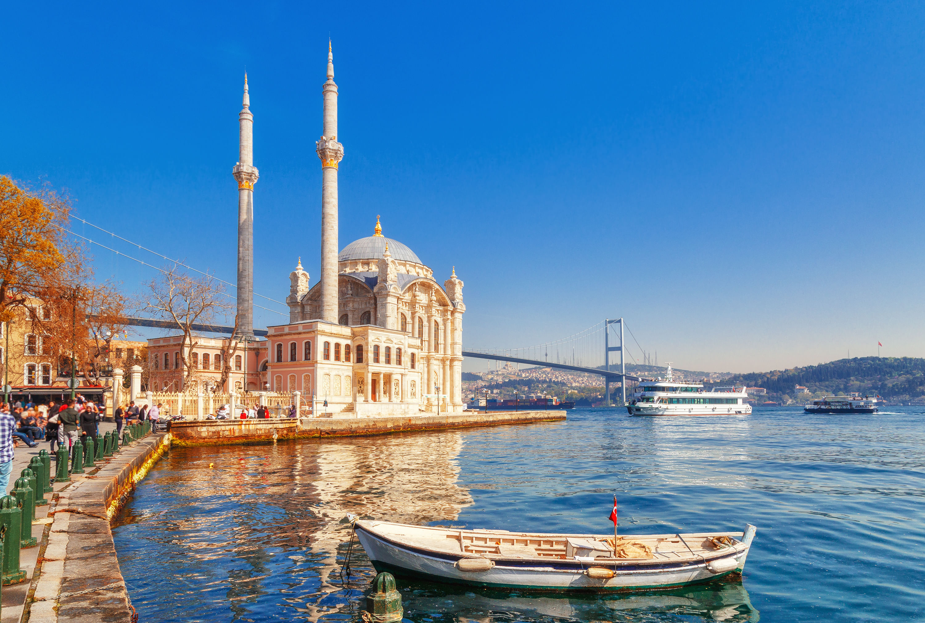 “Ortaköy Mosque located on the edge of the Bosphorus Strait, viewed from the water with boats passing and Istanbul’s city skyline behind.”