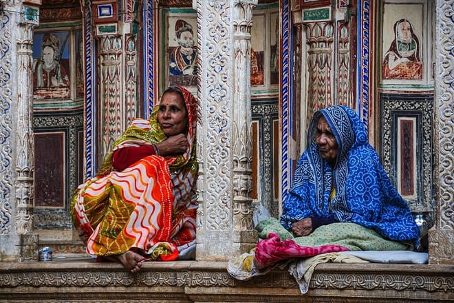 Women dressed in traditional sari sitting in front of a haveli of in Mandawa Town Rajasthan