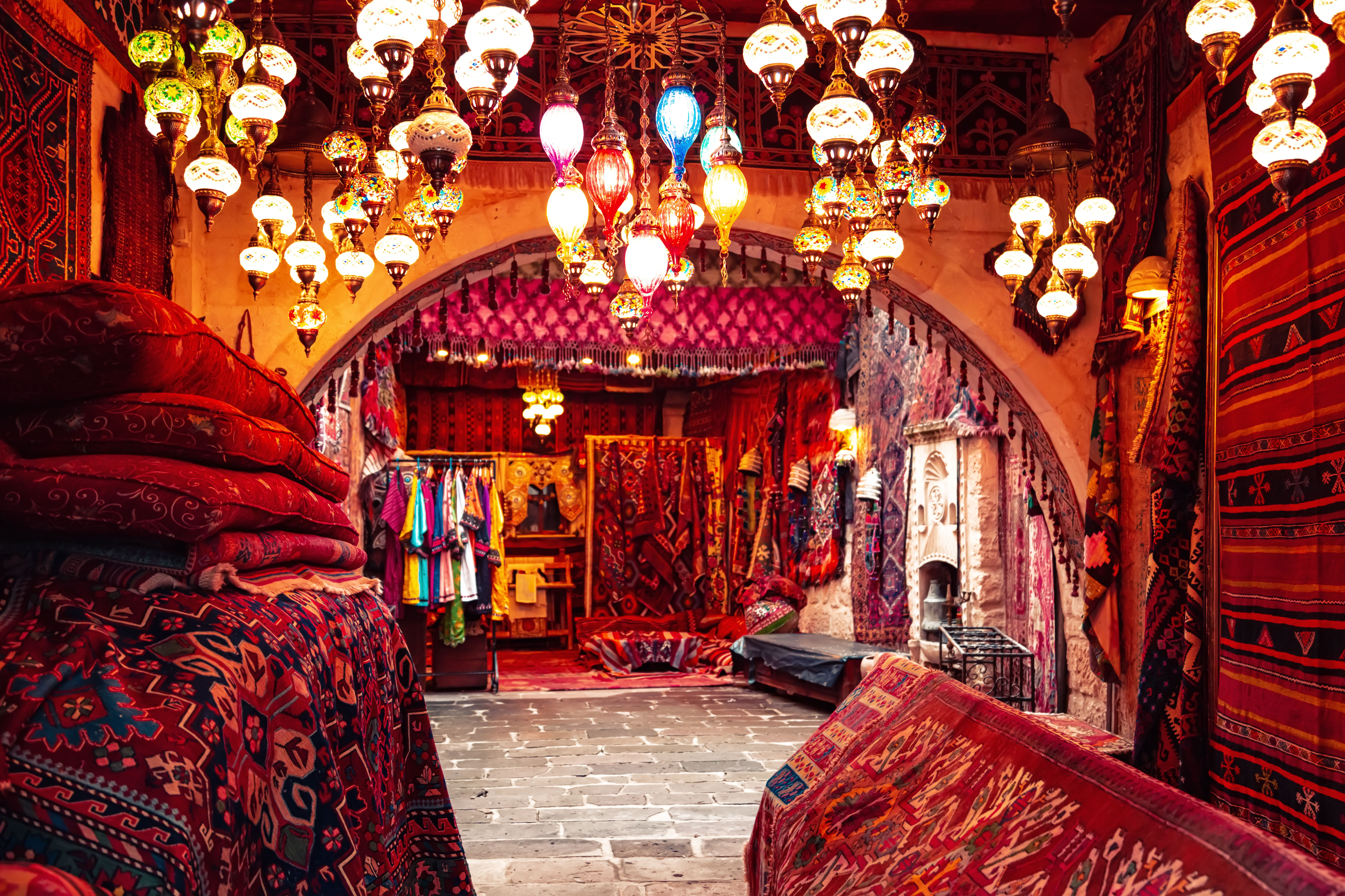 “Interior of a Grand Bazaar carpet shop filled with colorful, intricately patterned Turkish carpets and rugs hanging on the walls and stacke