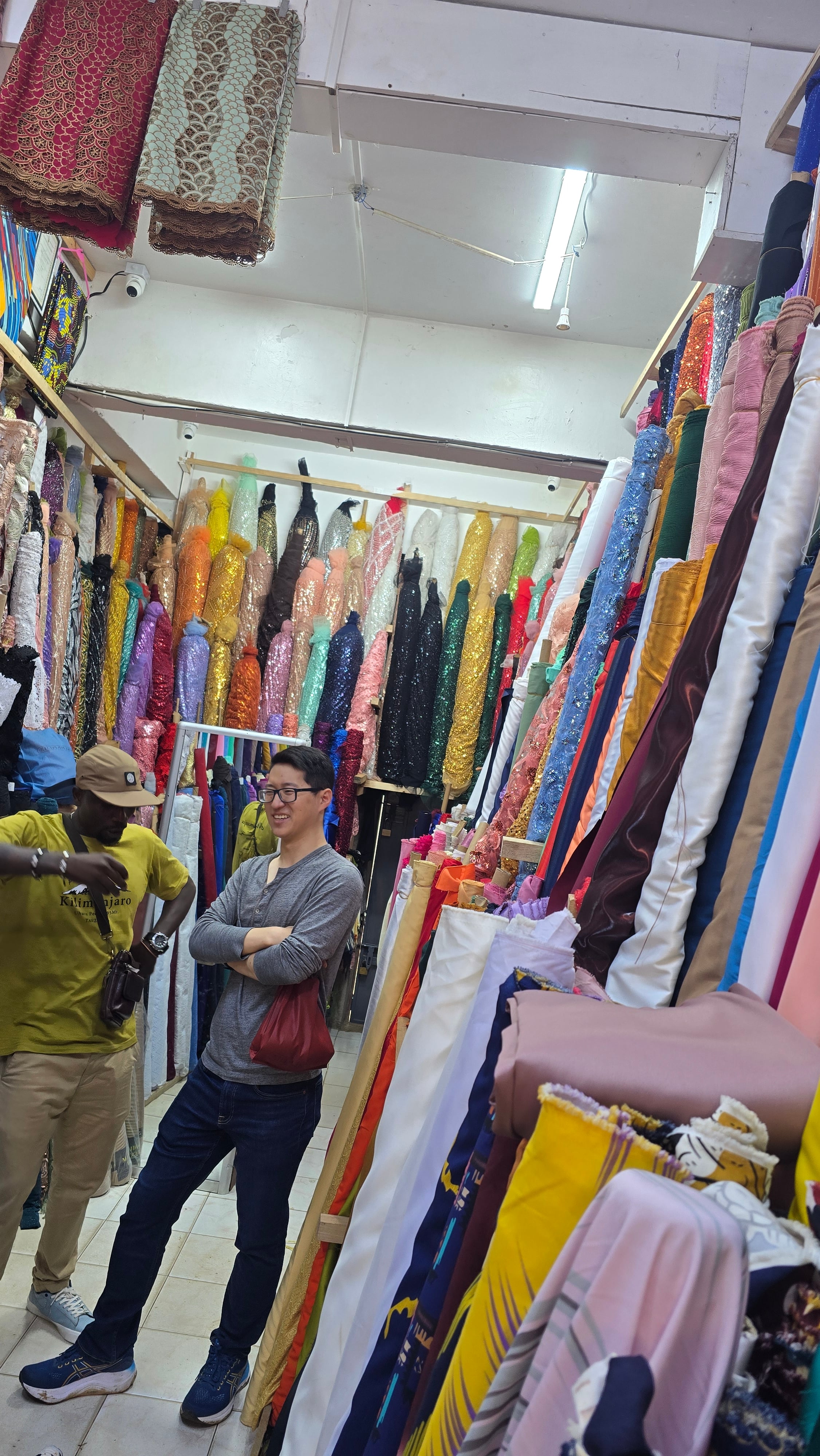 A guide and traveler visiting a textile stall filled with colorful African fabrics in Moshi.