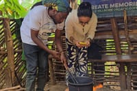 A local guide and a tourist stirring coffee beans in a traditional pot over a fire pit in Tanzania.