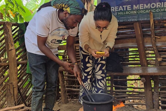 A local guide and a tourist stirring coffee beans in a traditional pot over a fire pit in Tanzania.