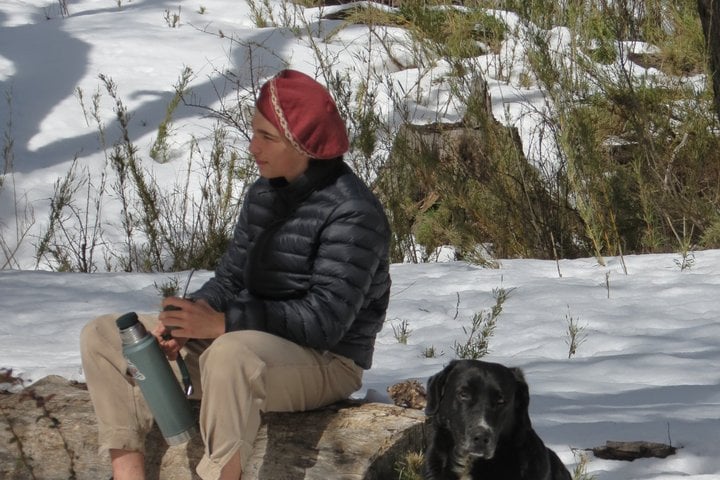 Traveler enjoying a hot drink with the tour dog during a break in the snowy forest on the San Martín de los Andes 4x4 tour