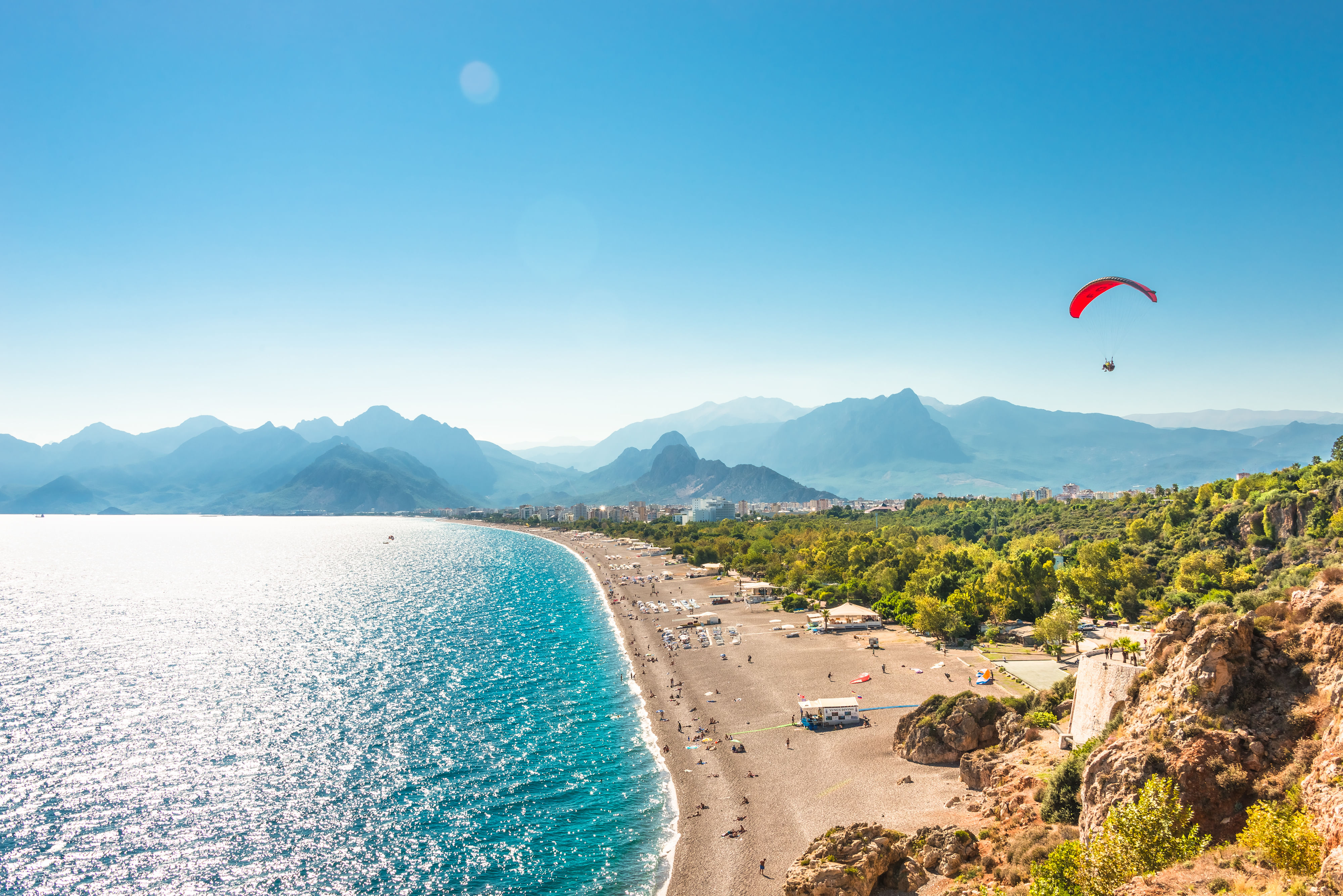 “Bird’s-eye panoramic view of Antalya with the city nestled between green hills and the turquoise waters of the Mediterranean Sea.”