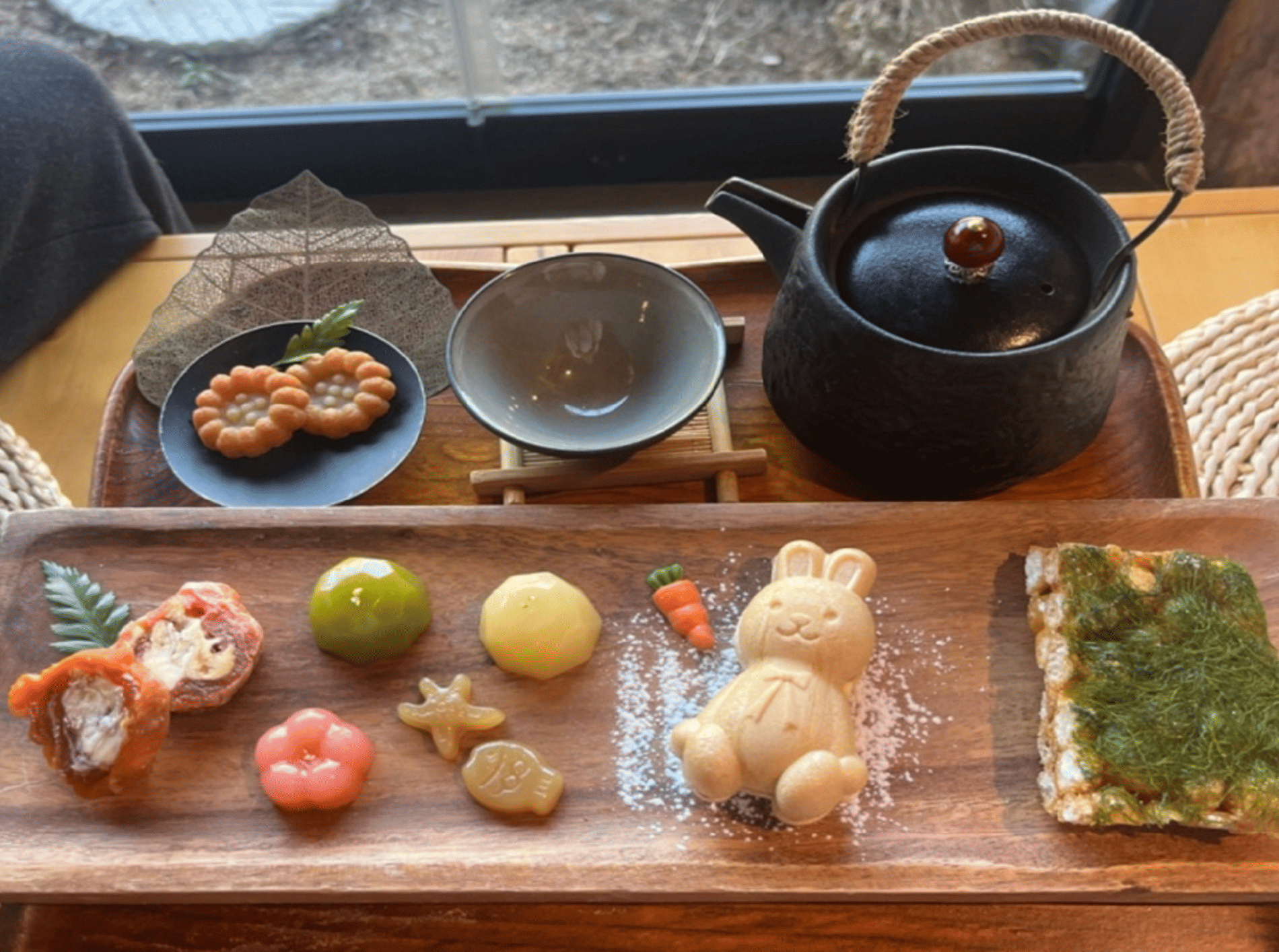 A tray of Korean traditional desserts shaped like fruits and animals, served with tea at a cafe.
