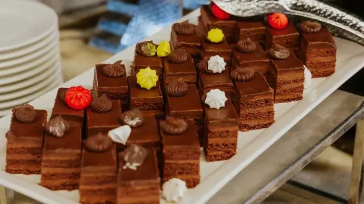 A long platter filled with small chocolate cakes topped with colored decorations sits on a table at Alexandra Sea Lounge.