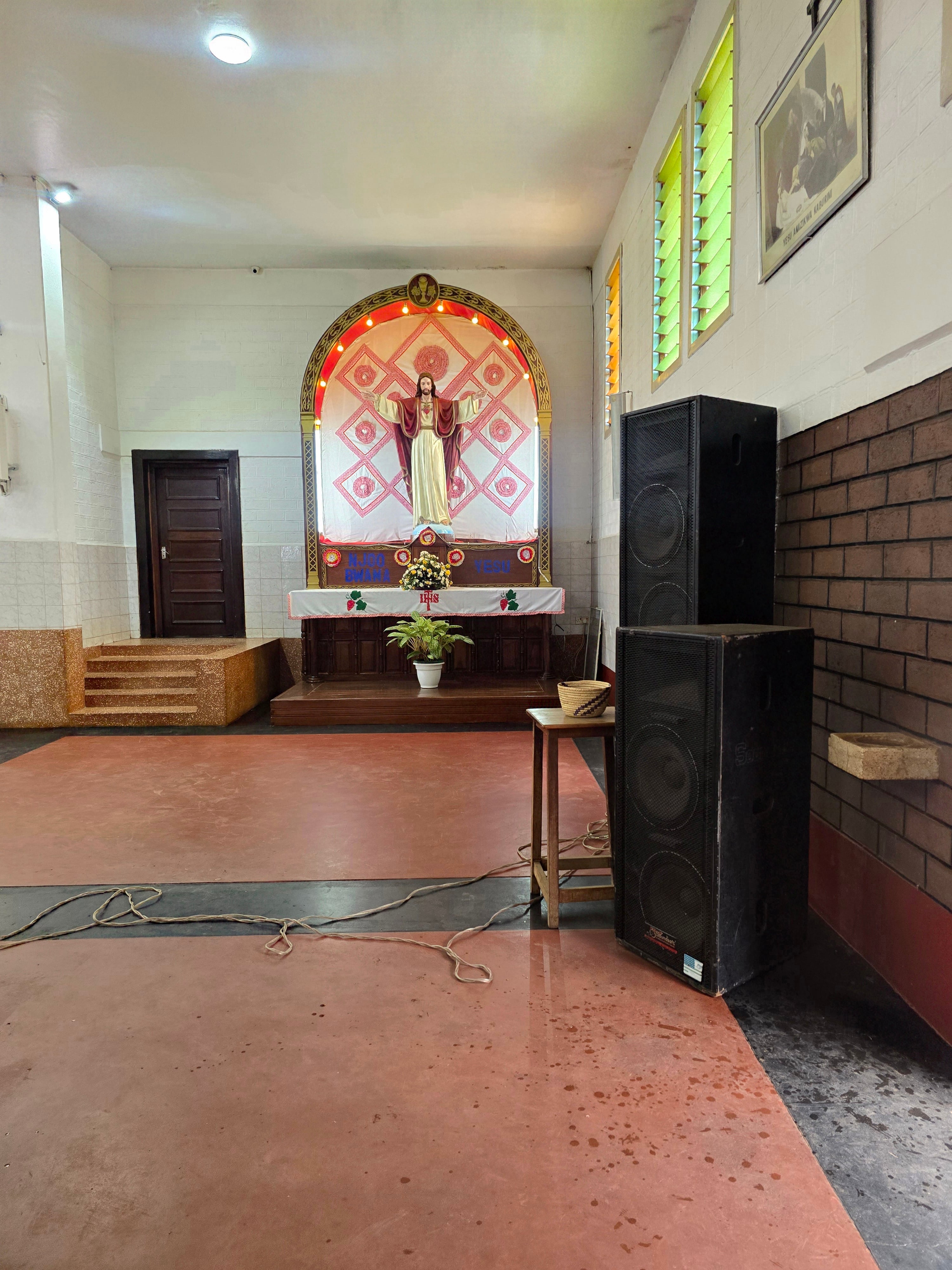 A view of the church altar featuring ornate religious backdrop designs, a central cross, and speaker equipment on the side.