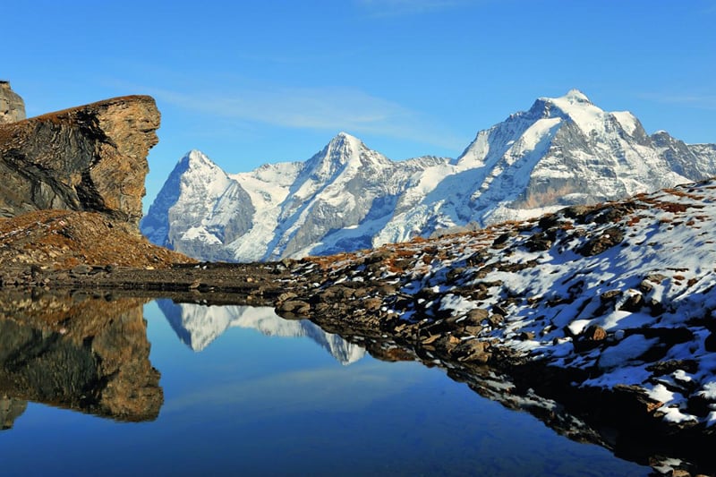 Um lago de montanha acima de Mürren no outono, com o Eiger, o Mönch e a Jungfrau refletidos na água.