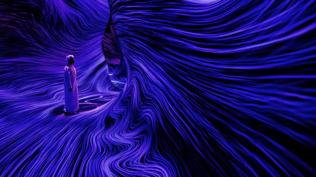 A person in white stands inside a dark, cave-like corridor illuminated by sweeping purple and blue light lines at TeamLab Phenomena.