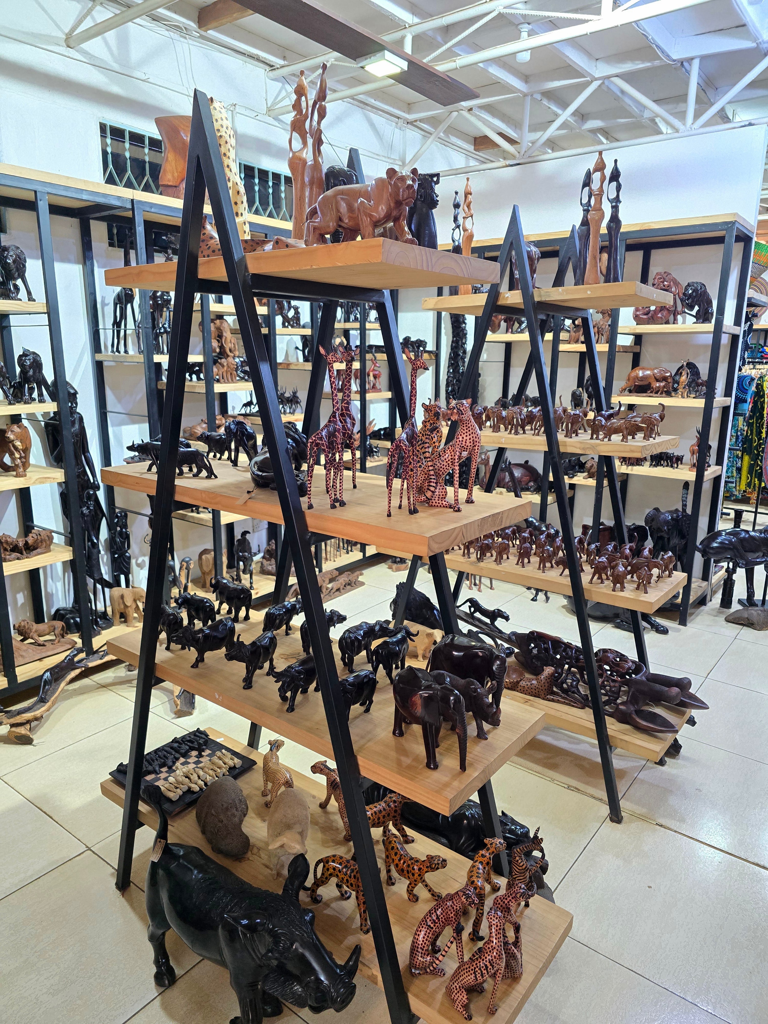 Multi-tiered wooden stands showcasing artisanal hand-carved wildlife figurines and cultural sculptures inside a souvenir shop.