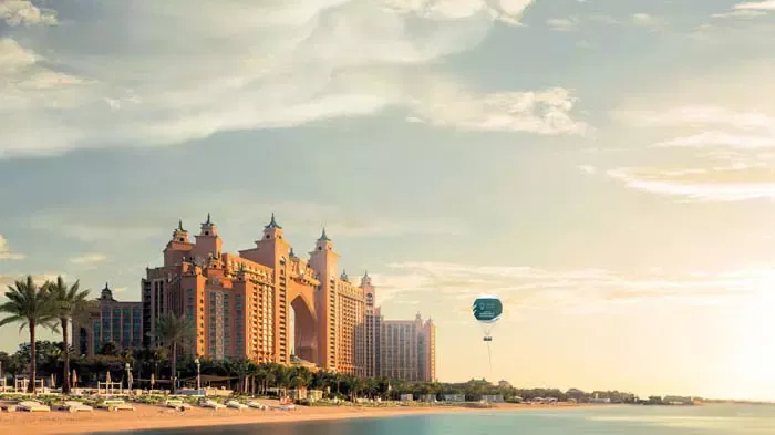 A large tethered green and white balloon floats above a resort hotel and beach at The Dubai Balloon at Atlantis.