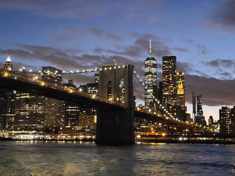Brooklyn Bridge and Manhattan skyline lit up at dusk over East River