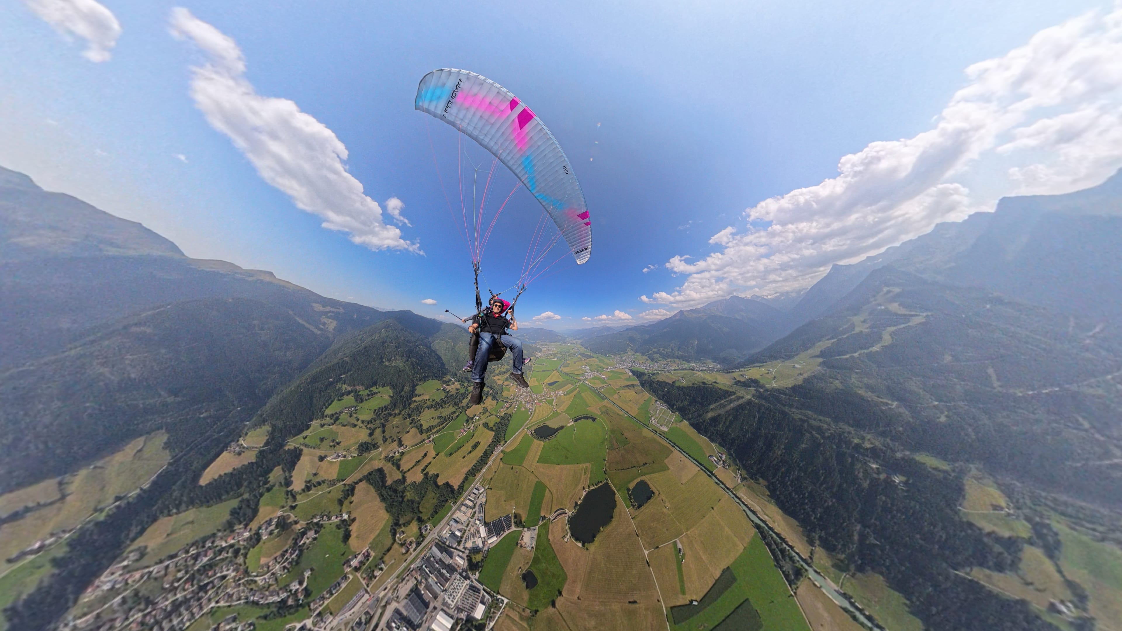 A male passenger paragliding with a female tandem pilot high above a wide alpine valley in Austria