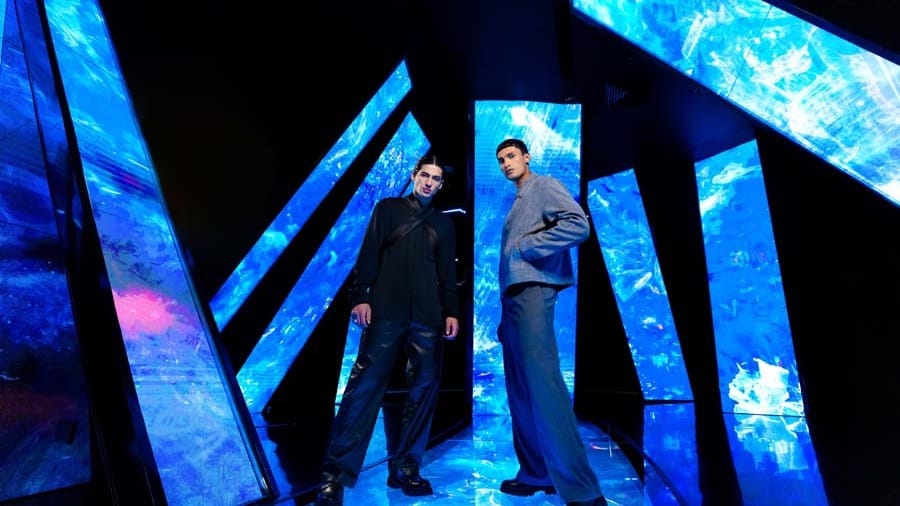 Two visitors among tall angled mirrored panels lit with bright blue ice-like patterns in an AYA Universe Dubai zone