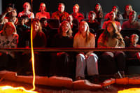 Audience members watch closely and take photos as a large, glowing blob of cooled lava rests on a sand platform in front of them.