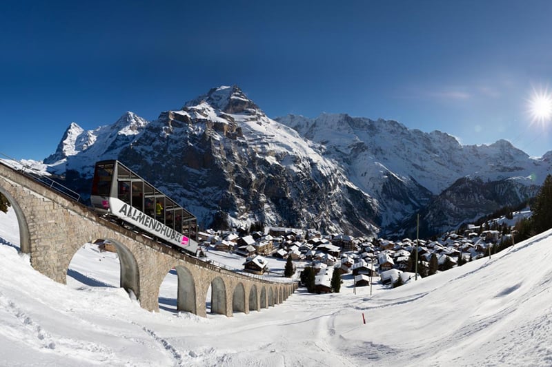 O funicular do Allmendhubel sobre o viaduto, com Mürren e os picos nevados.