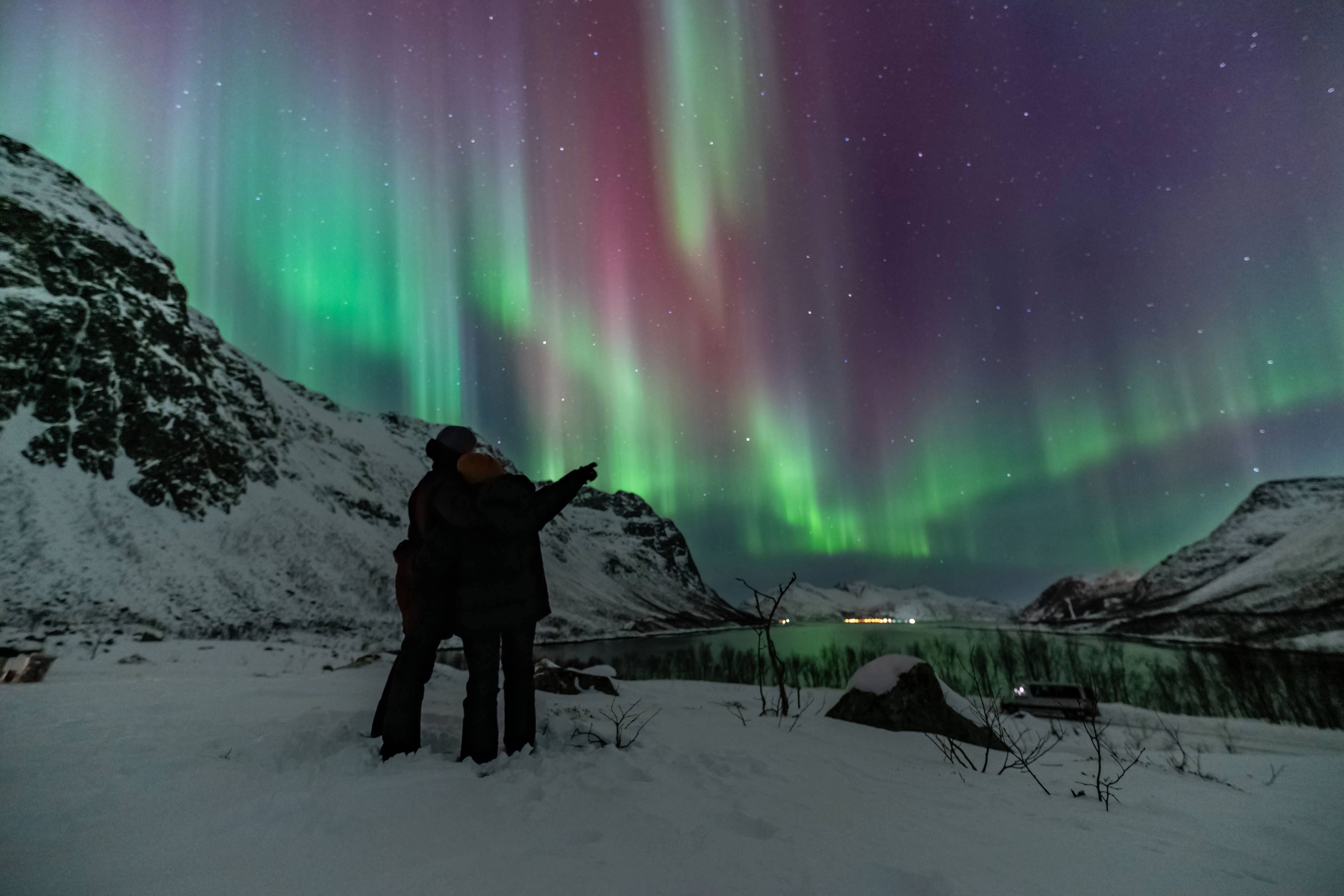 Couple pointing at a rare pink and green Northern Lights display over a snowy landscape on a private Tromsø Aurora tour.