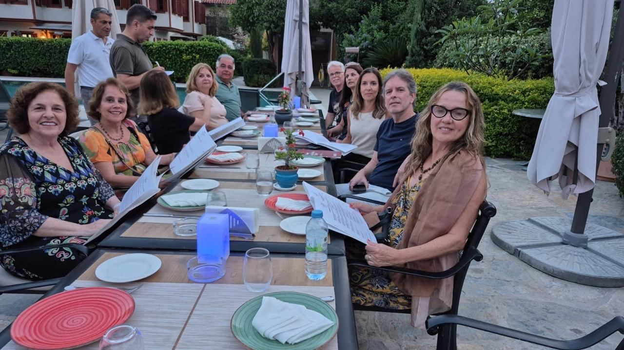 “A tour group sitting at an outdoor table with their guide, smiling and enjoying a lunch break together during the trip.”
