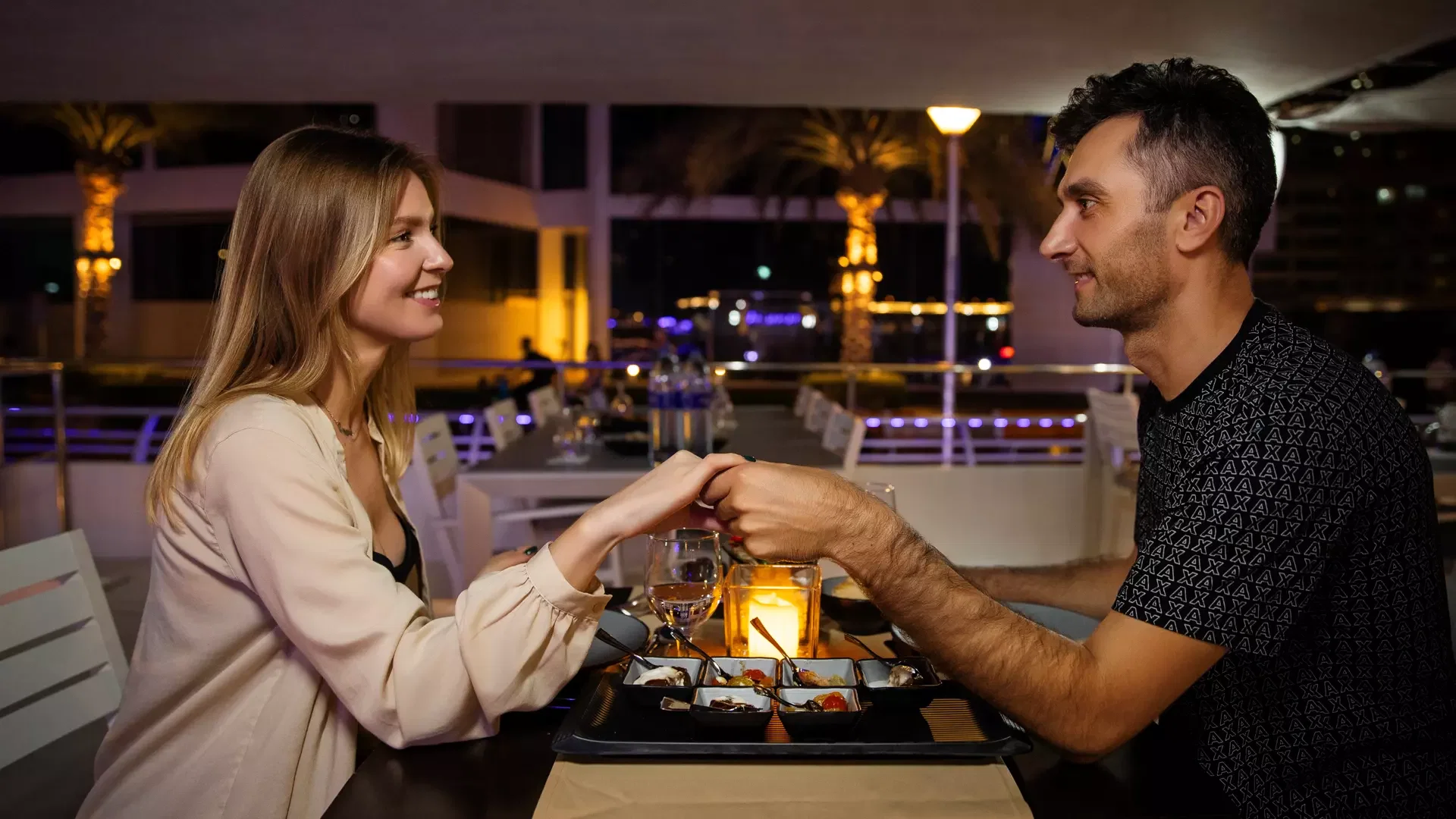 A smiling couple holds hands and gazes at each other across a candlelit table at Alexandra Sea Lounge.