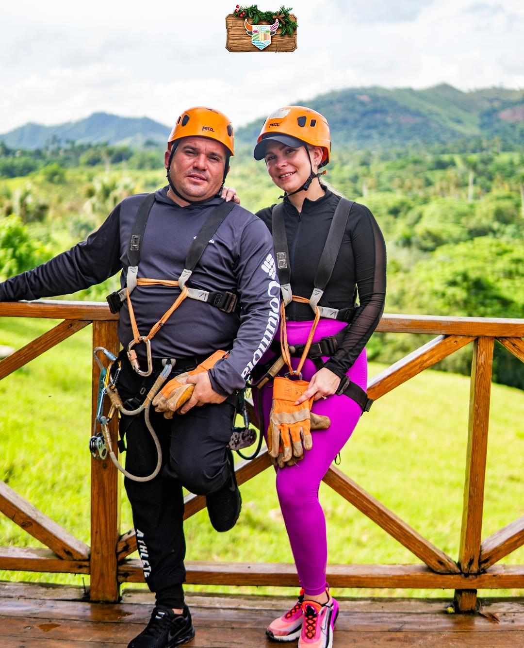 Man and woman wearing helmets and safety gear on a zip line platform in Punta Cana, ready to start their adventure, surrounded by lush mount