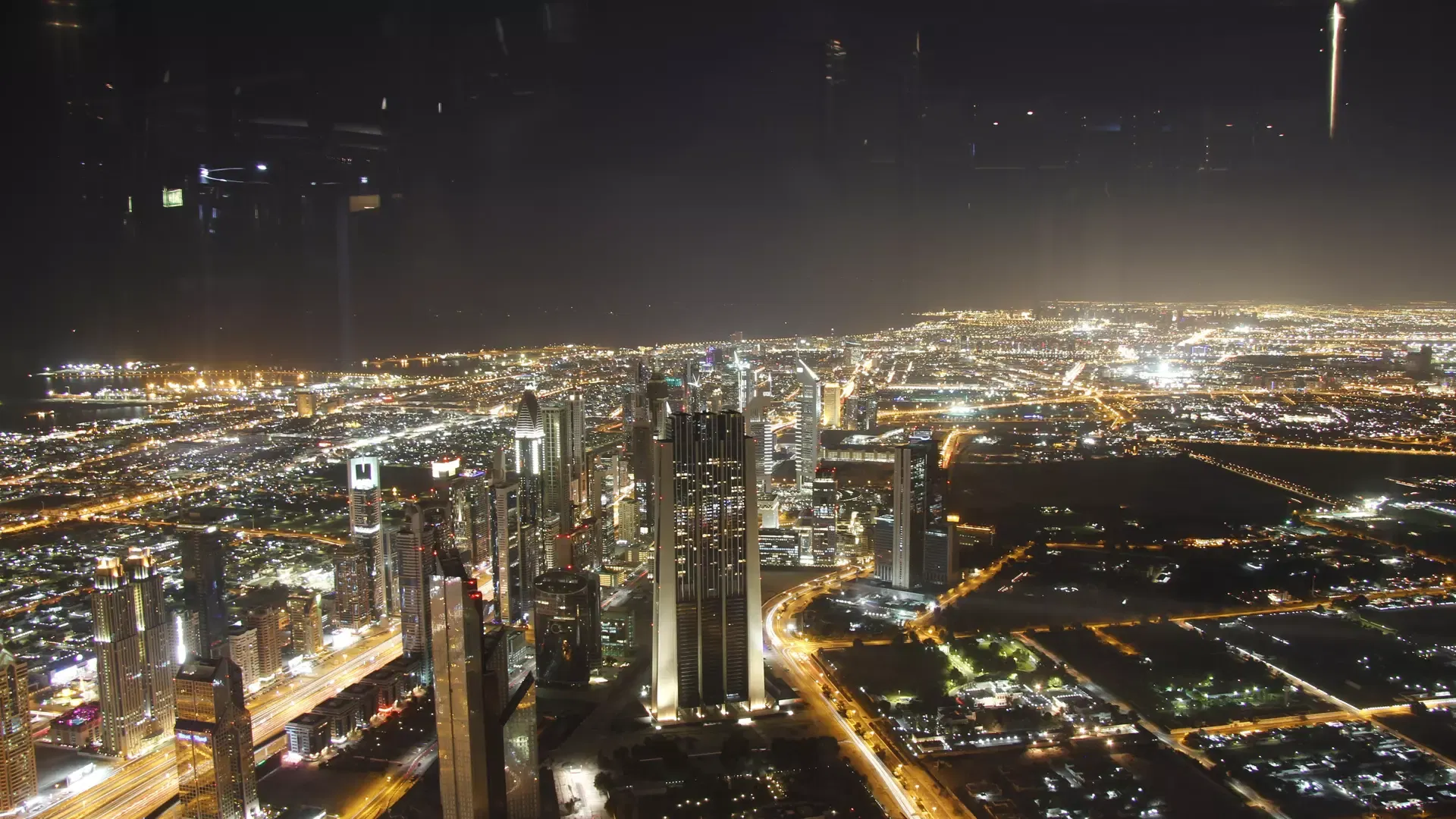 The lights of the Dubai coastline and the city stretching to the dark horizon on a clear night, seen from Burj Khalifa
