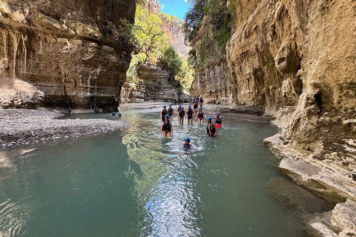 Group of people enjoying the turquoise river in Osumi Canyon with tall rock walls on each side.