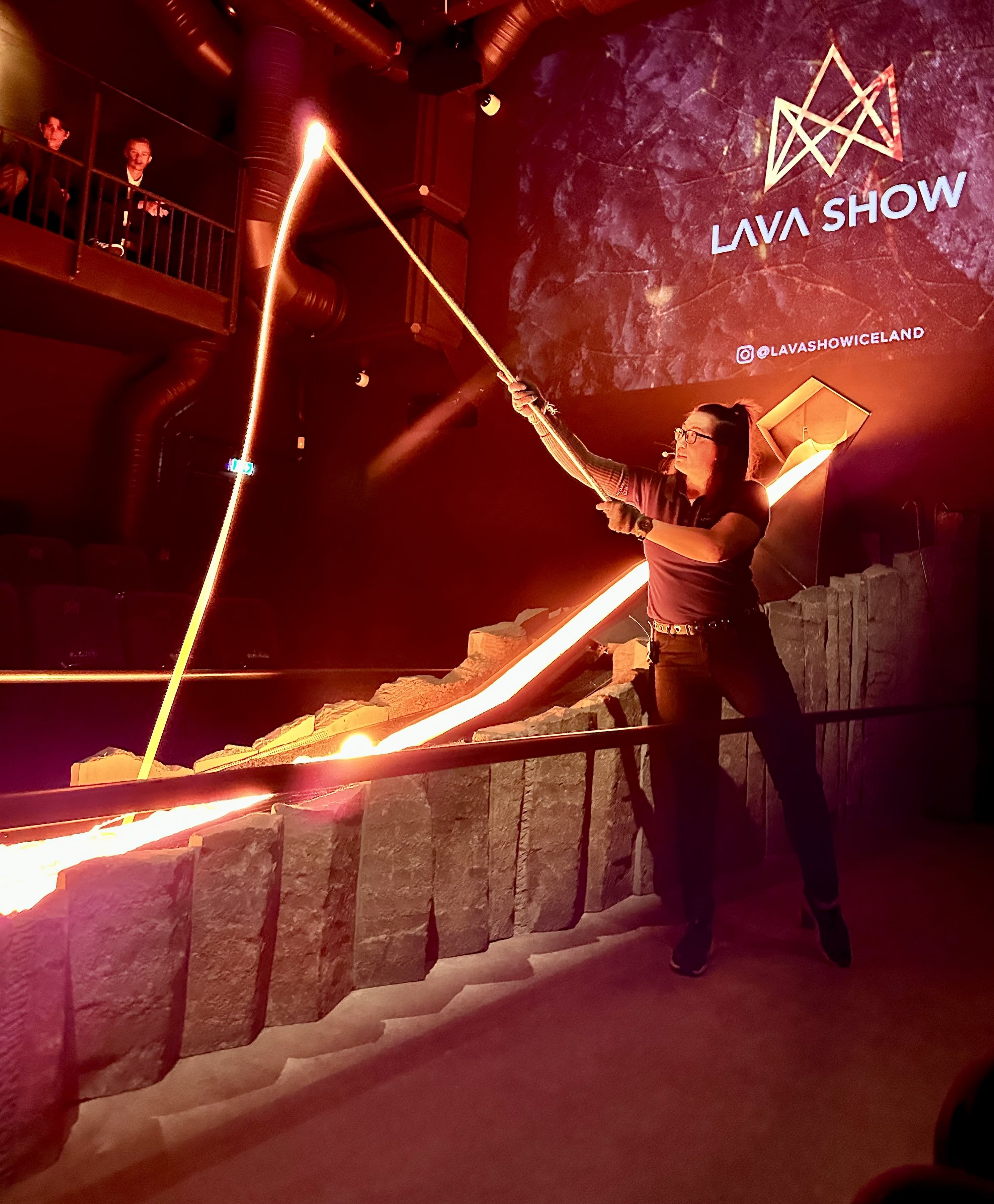 An overhead view of an audience seated around a lava channel in a dark theater, watching the glowing lava flow through the stage.
