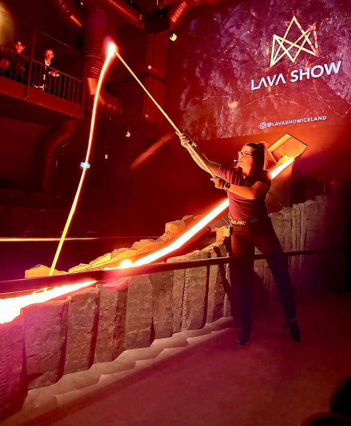 An overhead view of an audience seated around a lava channel in a dark theater, watching the glowing lava flow through the stage.