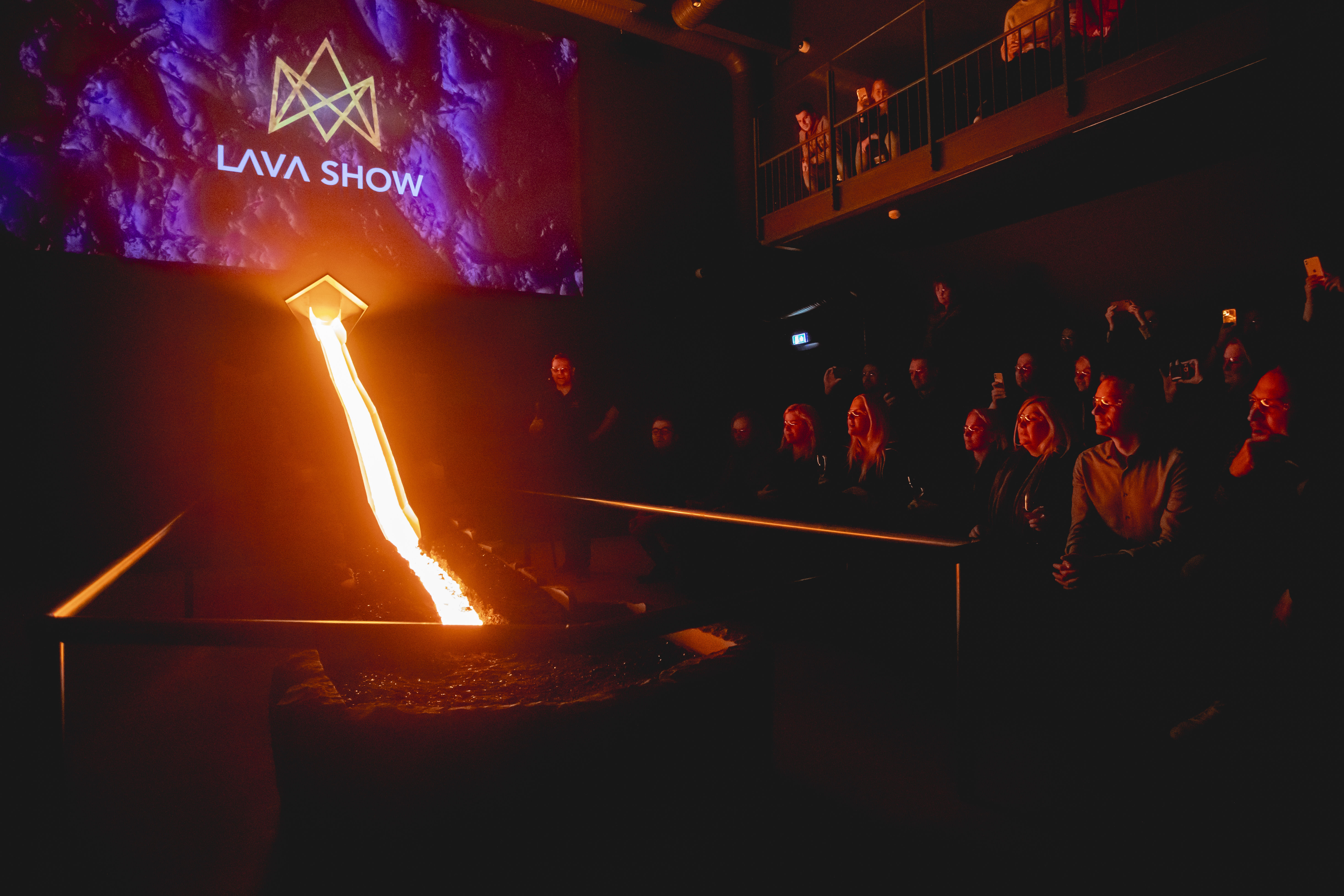 Molten lava flows down a steel channel in a dark showroom with the