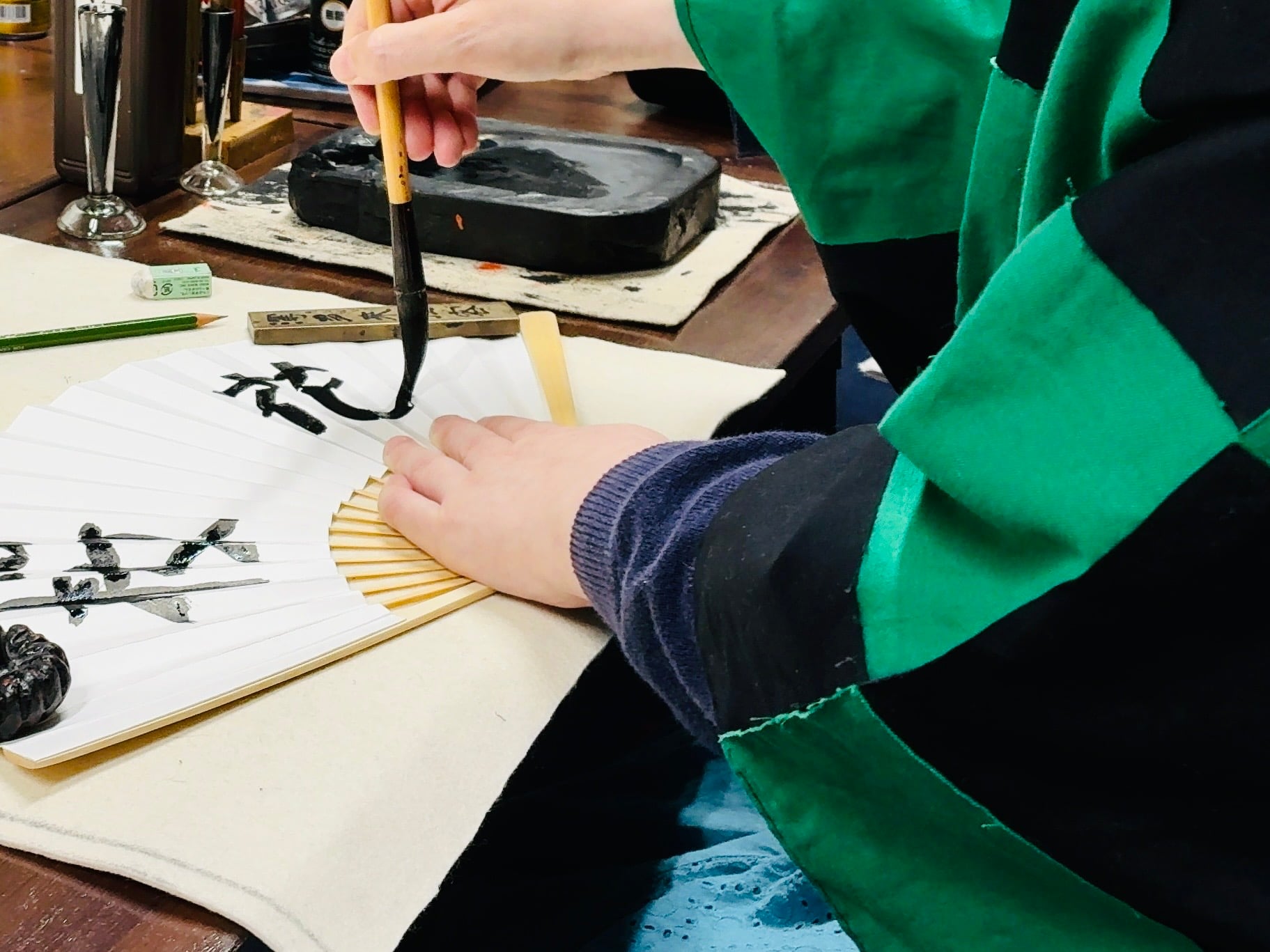 An international guest practicing Japanese calligraphy on a folding fan.