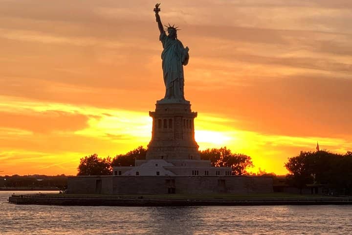 Statue of Liberty silhouetted against golden sunset over New York Harbor waters
