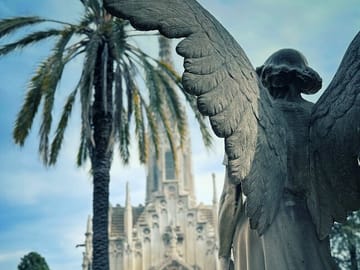 A view of one of the art nouveau mausoleums with an angel sculpture in the foreground on the montjuic cemetery tour