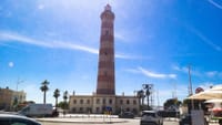 Barra Lighthouse near Aveiro with striped tower, palm trees, cars, and blue sky