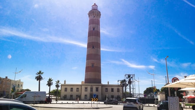 Barra Lighthouse near Aveiro with striped tower, palm trees, cars, and blue sky